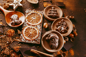 chocolate bar with orange. spices are sprinkled on the surface, orange citron and pieces of dark chocolate on a dark brown background.