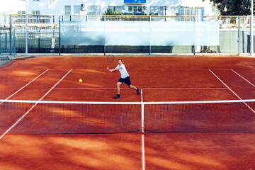 Man plays tennis on clay tennis field view from afar