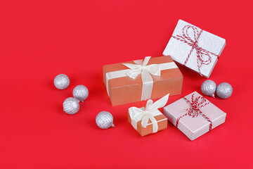 Four shimmering wrapped gift boxes with silver christmas balls on bright red background. New year celebration concept.