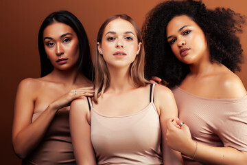Obraz premium young pretty asian, caucasian, afro woman posing cheerful together on brown background, lifestyle diverse nationality people concept