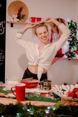 A nice, young blonde girl alone in a white shirt and jeans in the 
kitchen. The kitchen is decorated with New Year's decor. New Years 
is soon.