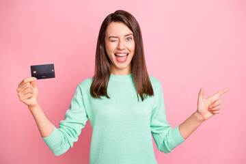 Fototapeta premium Portrait of positive funky brunette young woman point empty space wink promote credit card isolated on pink color background
