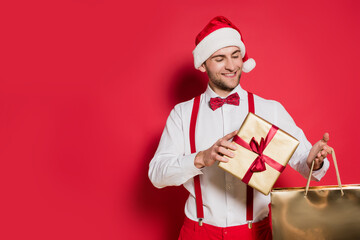  man in santa hat holding gift box and shopping bag on red background