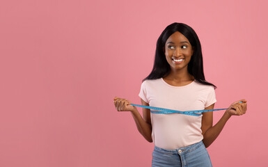 Slimming and body care. Black woman measuring her breast after weight loss diet over pink background, copy space
