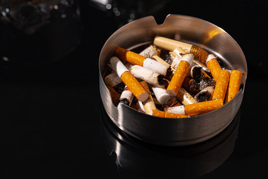 Ash tray full of cigarette butts on black background