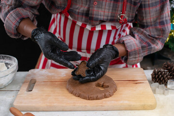 Male model in red striped apron preparing cookies, cut out gingerbread dough with biscuit moulds by hand, making Christmas cookies concept