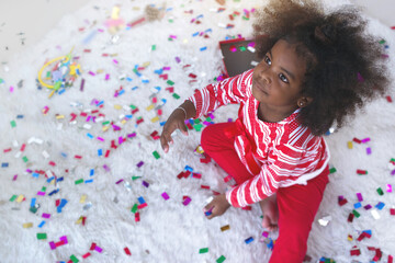 Obraz na płótnie Canvas Dark skinned little child girl sitting on the floor with confetti on background, new year or birthday party, Top view