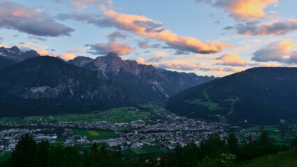 Beautiful panoramic view of city Lienz in Tyrol, Austria in valley after sunset in the evening light with illuminated clouds in the sky and majestic peaks of Gailtal Alps in background.