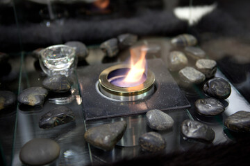 Bioethanol fueled portable fireplace burning at home, for live fire at home, no chimney and mantelpiece is needed. Liquid bio ethanol burns in cup. Round shaped glass with stones inside