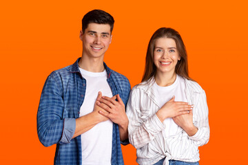 Grateful gesture concept. Pretty smiling young male and female in casual clothes keep hands on chest, being thankful
