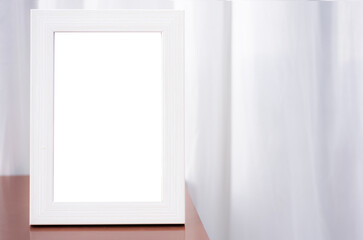 A blank white picture frame perched on the corner of the table. White curtain background in the room