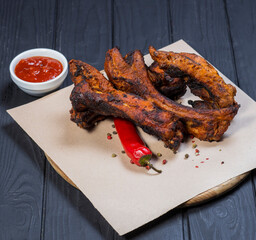 Grilled sliced barbecue pork ribs and tomato sauce on black wooden background, top view