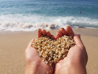 Mellow heart shaping female hands above sea and beach.