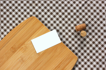 one empty business card, wine corks and cutting Board on a checkered tablecloth