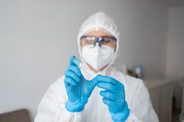 Medicine woman wearing protective gear, holding a test tube for 2019-nCoV analyzing. Coronavirus blood test concept. Selective focus