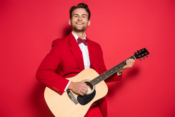  man in suit playing acoustic guitar on red background