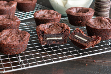 Oreo Stuffed Brownie Cups: Brownie cups filled with a sandwich cookie wire cooling rack with a bowl of frosting in the background