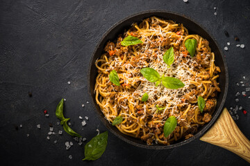 Pasta Bolognese, meat ragout in tomato sauce in the skillet at black table. Top view with copy space.