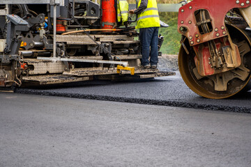 Industrial asphalt paver machine laying fresh asphalt on road construction site.