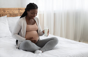 Calcium During Pregnancy. Black Pregnant Woman Sitting On Bed Holding Milk Glass