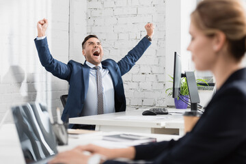  executive with yes gesture sitting at workplace with blurred colleague on foreground