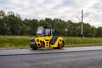 Fototapeta premium Asphalt road roller with heavy vibration roller compactor press new hot asphalt on the roadway on a road construction site. Heavy Vibration roller at asphalt pavement working. Repairing.