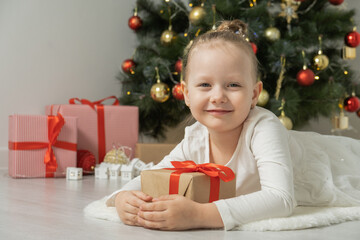 Cute little child girl lying on the floor near the Christmas tree with gift box.