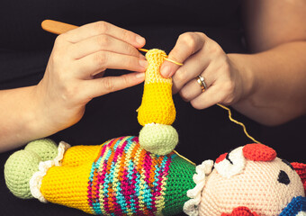 Hand of a woman using a knitting needle to sew a crochet clown doll. Handmade kids toy.