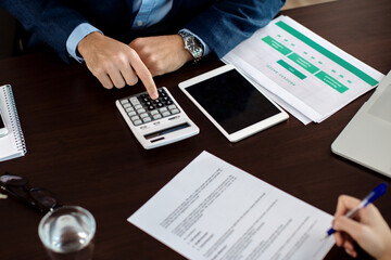 Close-up of financial consult using calculator while client is signing an agreement in the office.