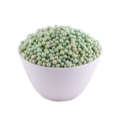 Green sugar dragee in white bowl isolated on white background, copy space.
