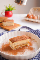 Traditional gourmet tiramisu Italian dessert topped with chocolate powder served on a white plate at table background