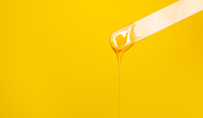 Sugar depilatory paste drips from a wooden spatula. The removal of body hair. Free space for text, yellow background.