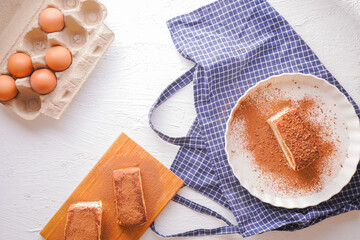 Delicious Tiramisu - traditional italian dessert from mascarpone cheese and biscuit. gourmet tiramisu dessert topped with chocolate powder served on a white plate at table background.