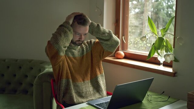 a man rubs his eyes with his hands from fatigue in front of the computer while working at home