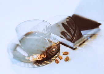 A cup of coffee with nuts and chocolate  in the glare of light on a white table
