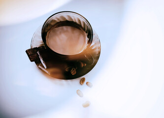 A cup of coffee with chocolate and nuts in the glare of light on a white table