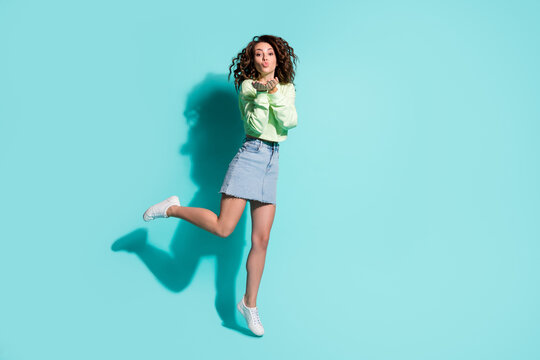 Full length body size photo of young girl jumping on one leg sending air kiss with pouted lips isolated on vivid teal color background