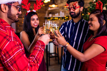 group of four indian friends cheering with champagne flutes and looking happy while having party on the kitchen at stay home quarantine corona virus outbreak party