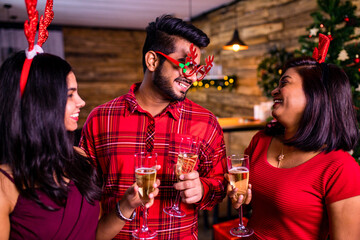 group of four indian friends cheering with champagne flutes and looking happy while having party on the kitchen at stay home quarantine corona virus outbreak party