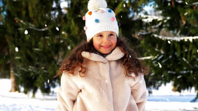 childhood, leisure and season concept - happy little girl throwing snow in winter park