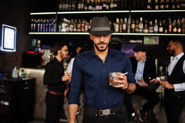 Stylish arab man against group of handsome retro well-dressed guys gangsters spend time at club, drinking on bar counter. Multiethnic male bachelor mafia party in restaurant.
