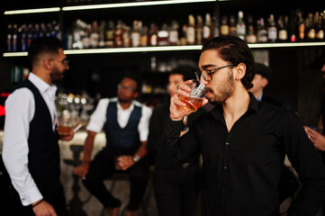 Stylish arab man against group of handsome retro well-dressed guys gangsters spend time at club, drinking on bar counter. Multiethnic male bachelor mafia party in restaurant.