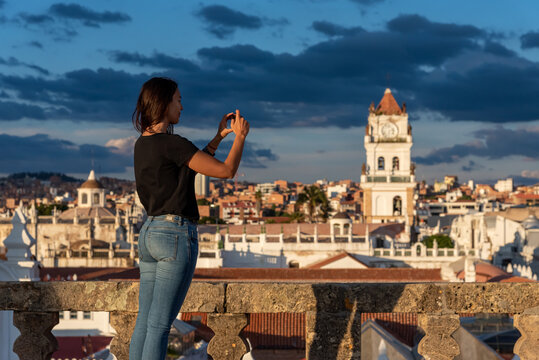 Woman taking pictures of the views over Sucre and its Belltower from a rooftop at Sucre, Bolivia