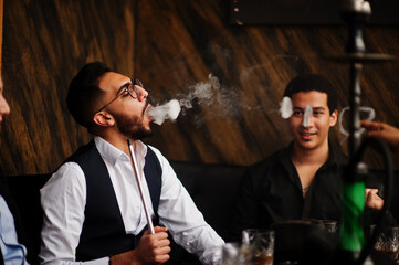 Group of handsome retro well-dressed man gangsters spend time at club, smoking hookah. Multiethnic male bachelor mafia party in restaurant.