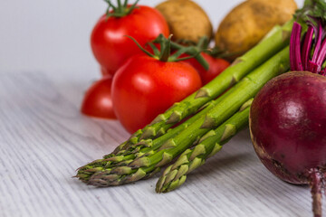 Variety of fresh and raw vegetables on a white wooden table. Beetroots, mushrooms, broccoli, asparagus, potatoes, sweet potatoes, and corn. Bright background. 