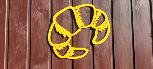 Yellow plastic croissant on a brown wall background. Room design.