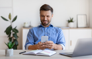Smiling Business Man Messaging On Smartphone While Relaxing At Workplace In Office