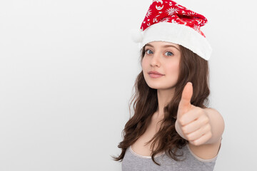 Girl in a santa claus hat showing thumbs up on a white background.