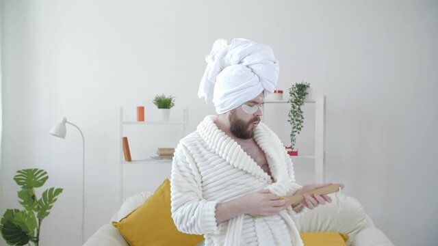 Carefree funny young man having fun dancing alone at home in a bathrobe and a towel on his head