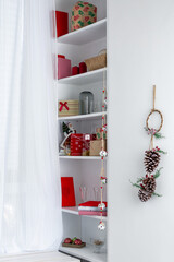 A window with white curtains and shelves on the sides that hold Christmas gifts.